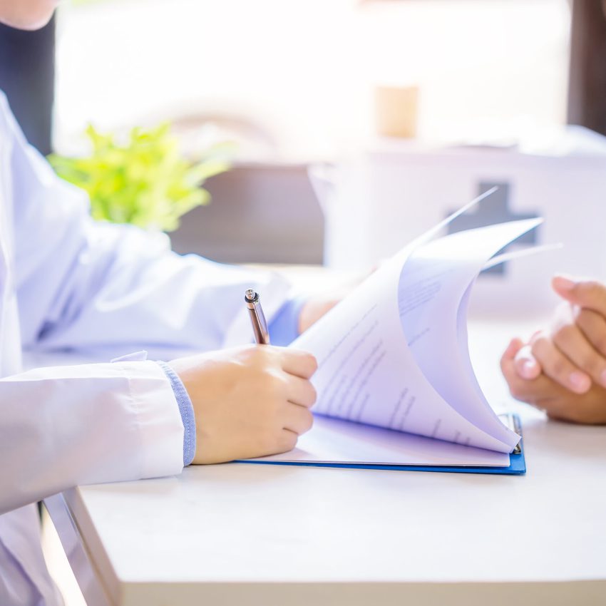 Doctor man consulting patient while filling up an application form at the desk in hospital. Medicine and health care concept