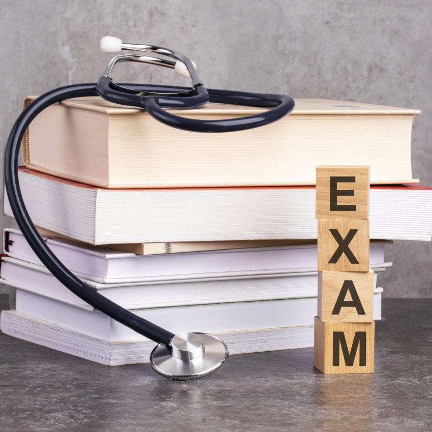 the word exam is written on wooden cubes near a stethoscope on a paper background. concept of medical education with book and stethoscope.